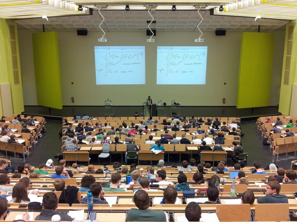 A overhead view of a college lecture hall with two video screens on the stage.
