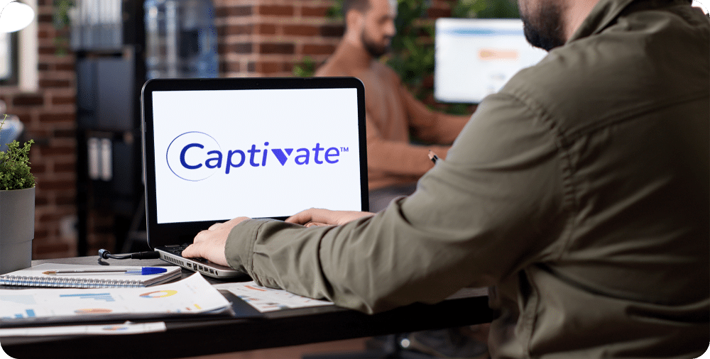 Man sits at an open laptop, on the screen is the word 'Captivate TM'