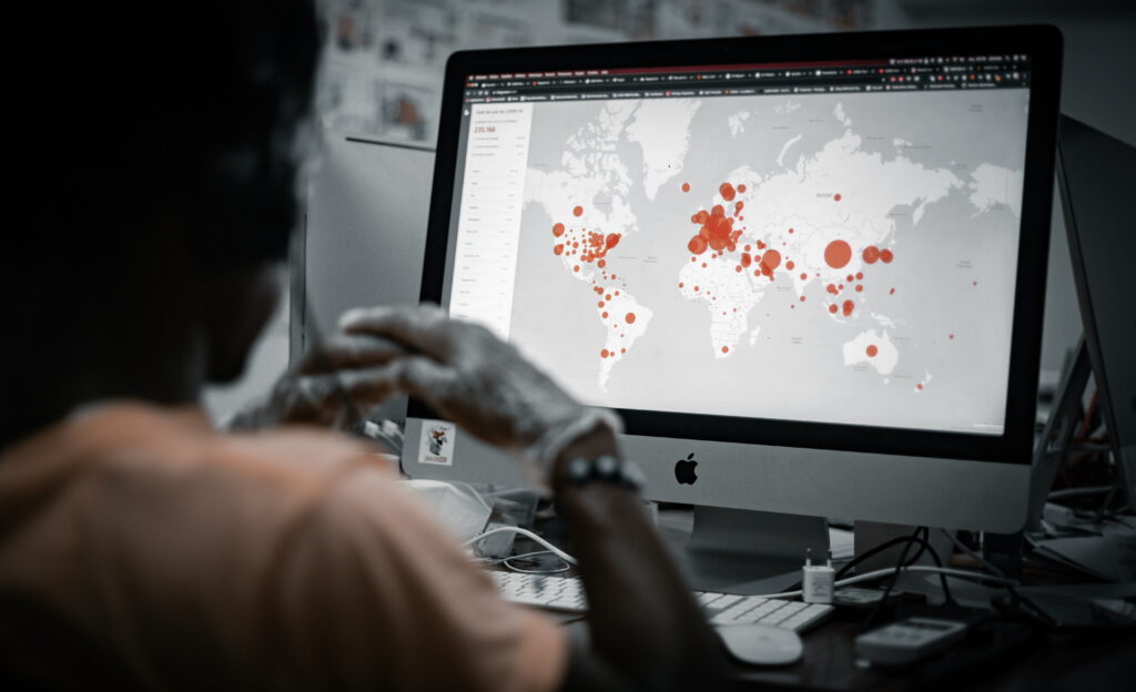 The back of a man sitting in front of an Apple monitor which showcases a global map view with orange touchpoints in multiple locations