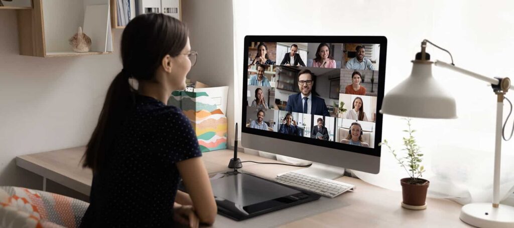 A woman with brown hair in a pony tail is shown participating on a webinar with many attendees on her screen.