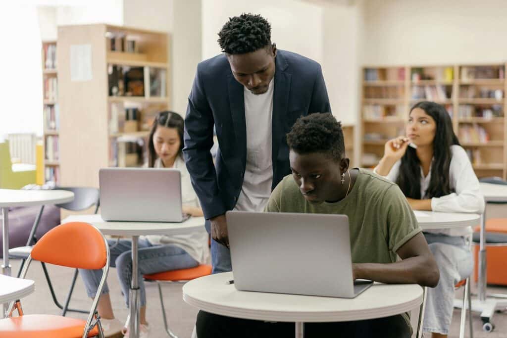 A teacher looks over the shoulder of a student working on his laptop