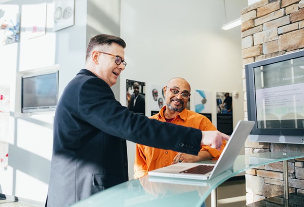 Two men look at an open laptop on a desk.