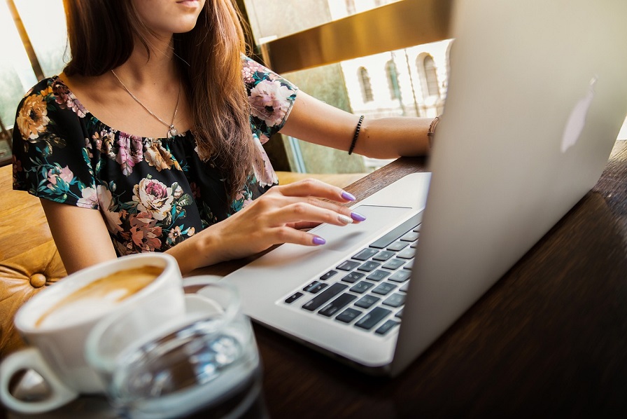 A woman with dark hair and a floral print blouse uses a laptop at a desk