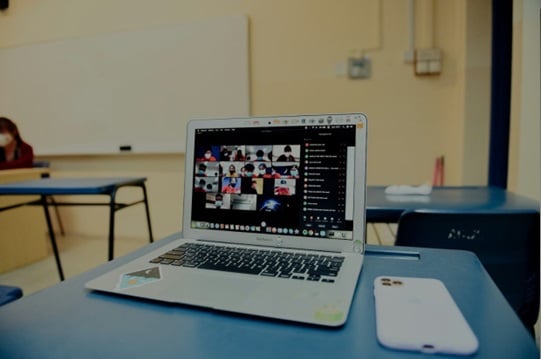 An open laptop sits on a blue-topped desk. A mobile phone sits next to it