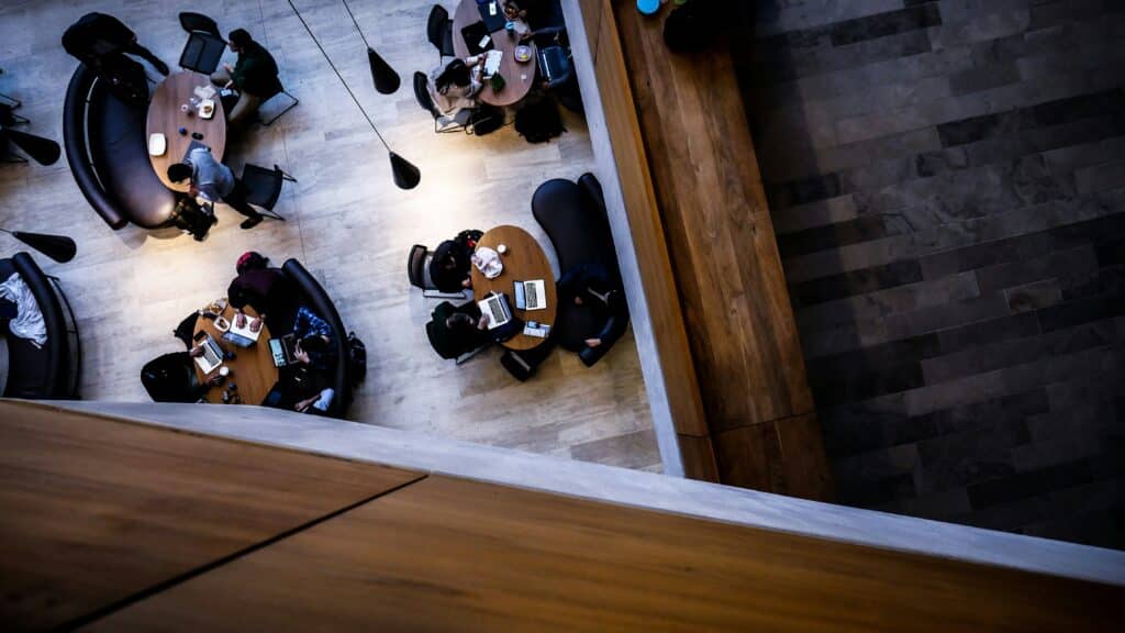 A bird's eye view of students in a library setting working on laptops from circle tables