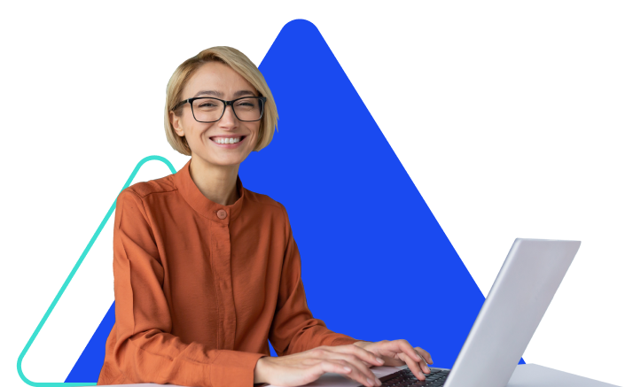 A professionally dressed woman in an orange buttoned shirt with short blonde hair and black glasses smiles at the camera while working from a laptop