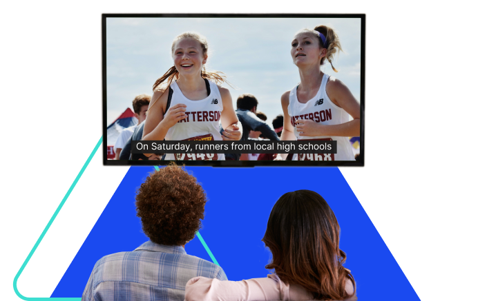 A man and a woman sit on a couch and watch television. On the screen are two female runners competing in a race.