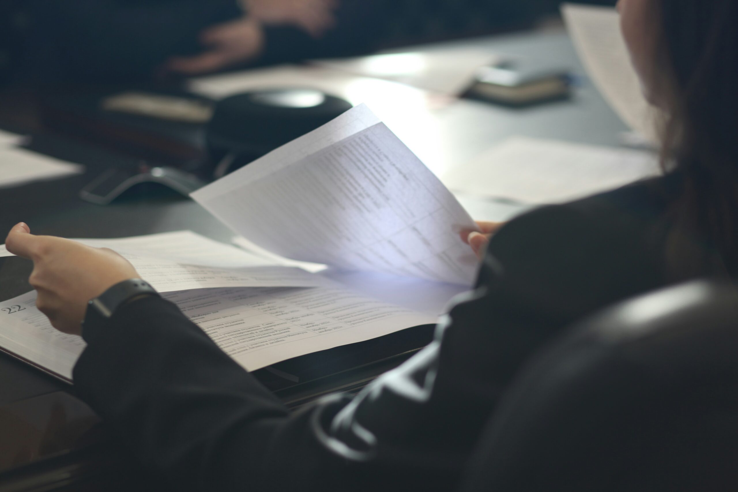 Over-the-shoulder view of a person flipping through financial reports on a conference table.