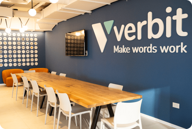 Tables and a chairs line the wall at the Verbit offices. The walls are dark blue and the words 