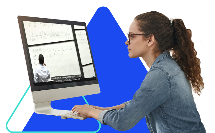 A woman with brown hair and glasses wearing a denim shirt works on her desktop computer.