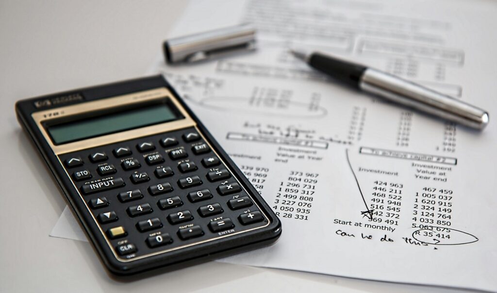 A black calculator sits atop a piece of paper containing numbers and equations.