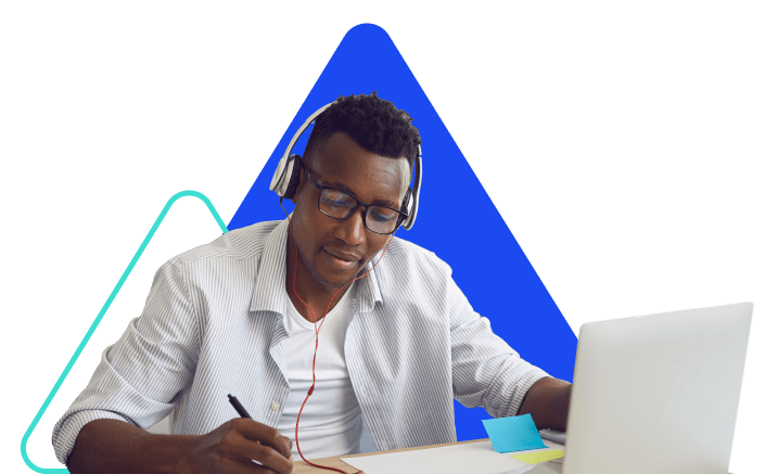 A man with dark hair wearing glasses and headphones sits at an open laptop.