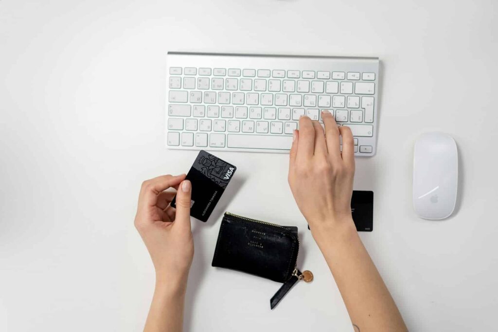A pair of hands, seen from above. In one hand is a credit card, the other hand types on a white keyboard.