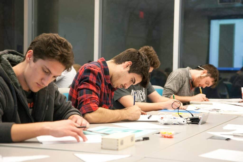 Students sit in a row at a table working on class assignments