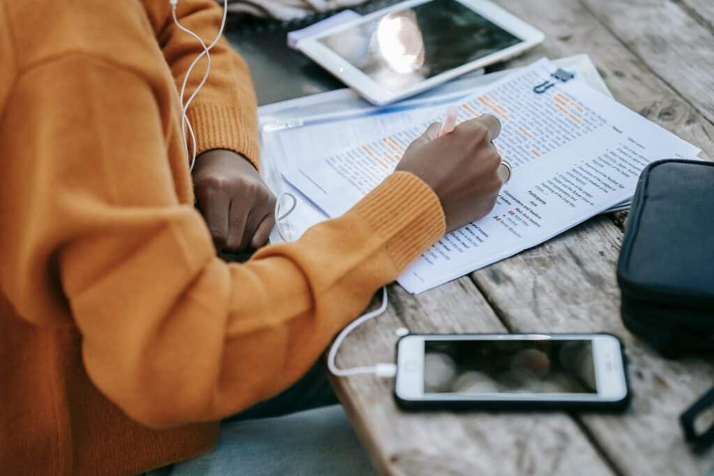 A person works at a desk. A tablet is at one of the desk, a cell phone with headphones is positioned at the other