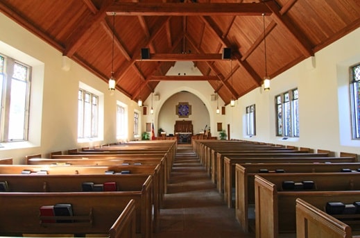 Looking down the center aisle inside a house of worship. Rows of pews line the aisle.