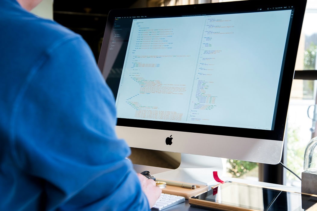 Over-the-shoulder view of a person wearing a blue shirt working on a desktop computer.