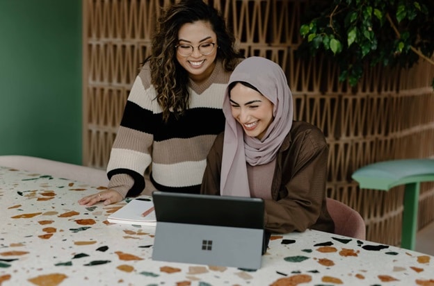 Two women smile as they look at the screen of a laptop.