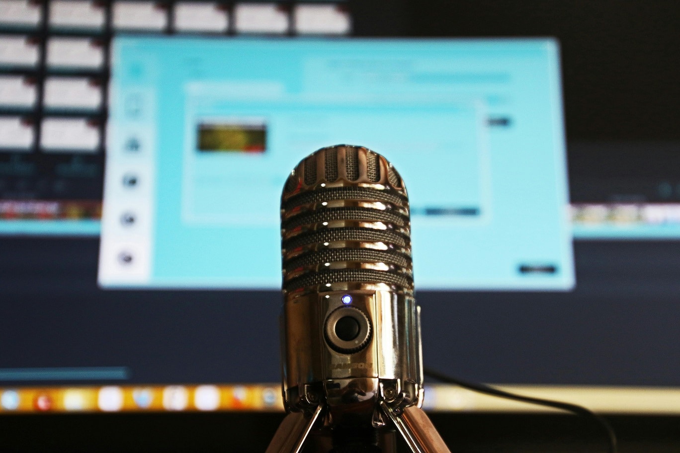 A silver microphone is positioned in front of a blurred computer screen.