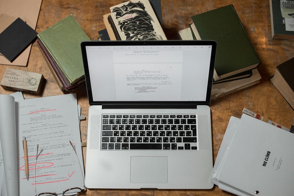 overhead view of an open laptop with paper and books scattered around.