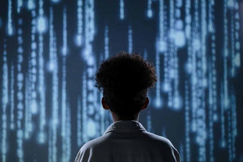 A young person stands in silhouette in front of a screen of dripping blue lights that denote technology