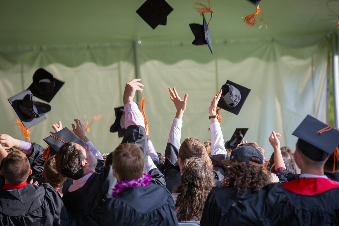 Viewed from behind, students in graduation gowns tossing their hats into the air