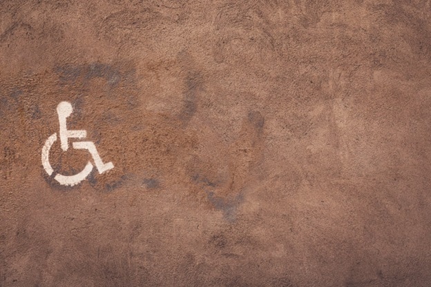 A white handicapped icon, slightly off center, is seen against a light brown background