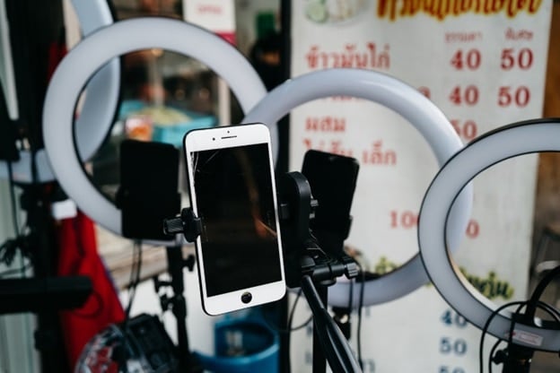 An iPhone rests in a crable in front of series of lights in a makeshift social media studio