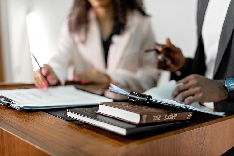 close up of lawyers working at a desk, a stack of legal books sit in the foreground