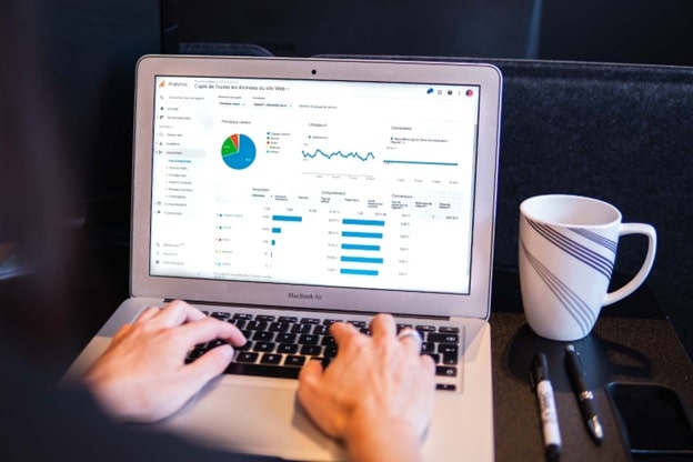 A pair of hands rest on the keyboard of an open laptop. On the screen are a series of charts and graphs.