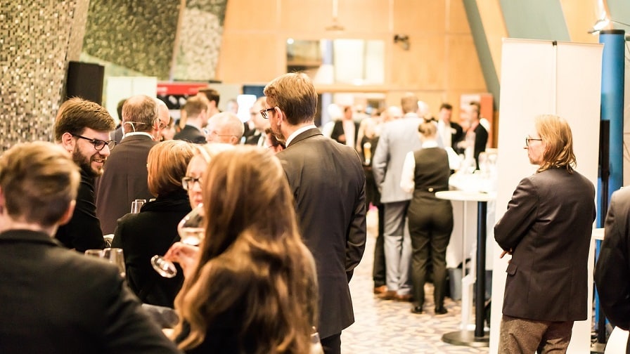 A wide shot of people dressed in business clothes standing and talking at a conference