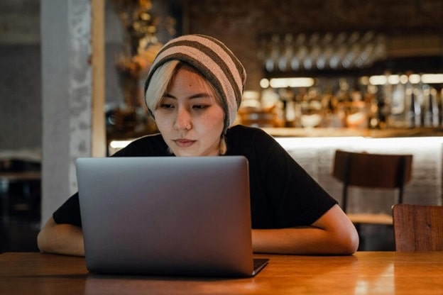 A young woman wearing a wool cap watches a program on her laptop.