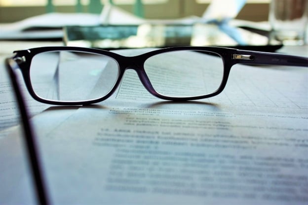 A pair of eyeglasses are seen laying on a document on a desk.