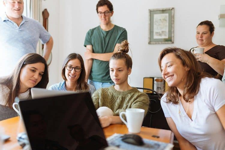 A group of people sit around a desk and watch video on a laptop screen.