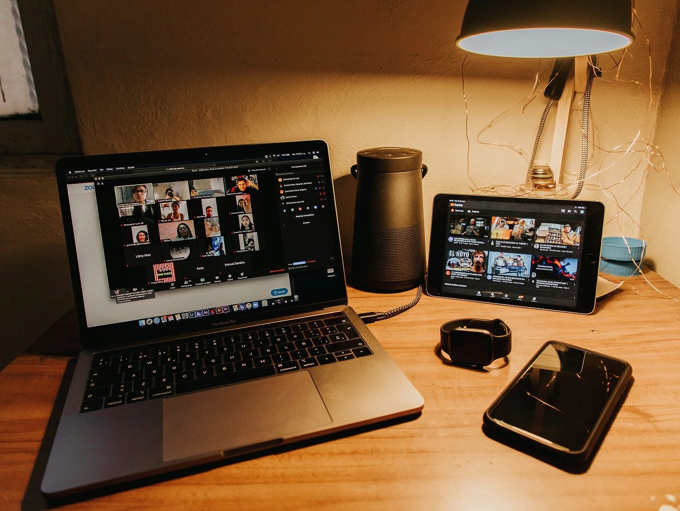 A laptop, tablet and phone sit on a desk. A virtual meeting is shown on the tablet and laptop screen.