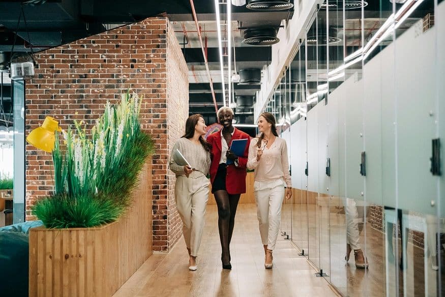 Three women walk down an office workplace hallway towards the viewer.