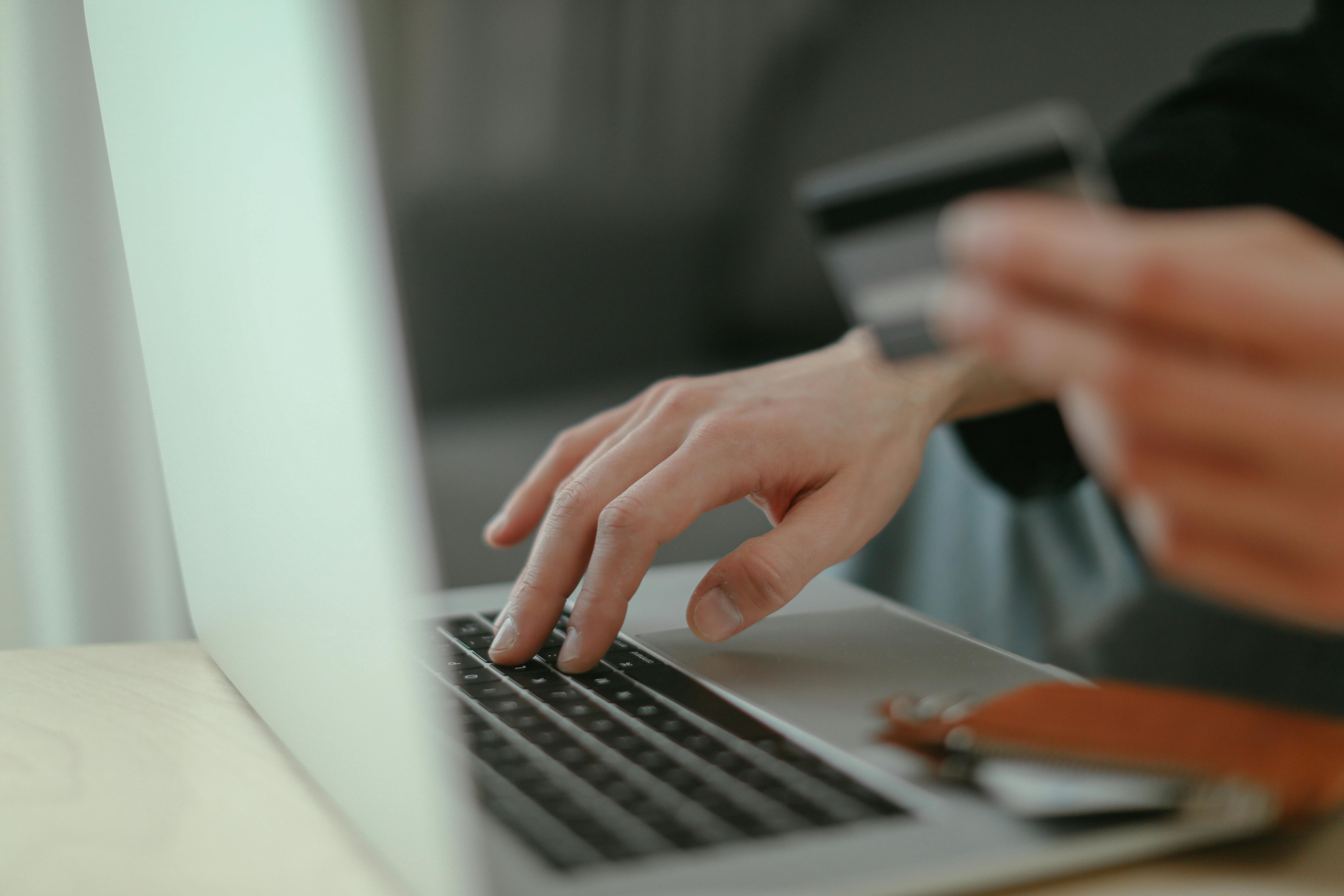 Close up view of a person online shopping, with one hand on a keyboard and the other holding a payment card.
