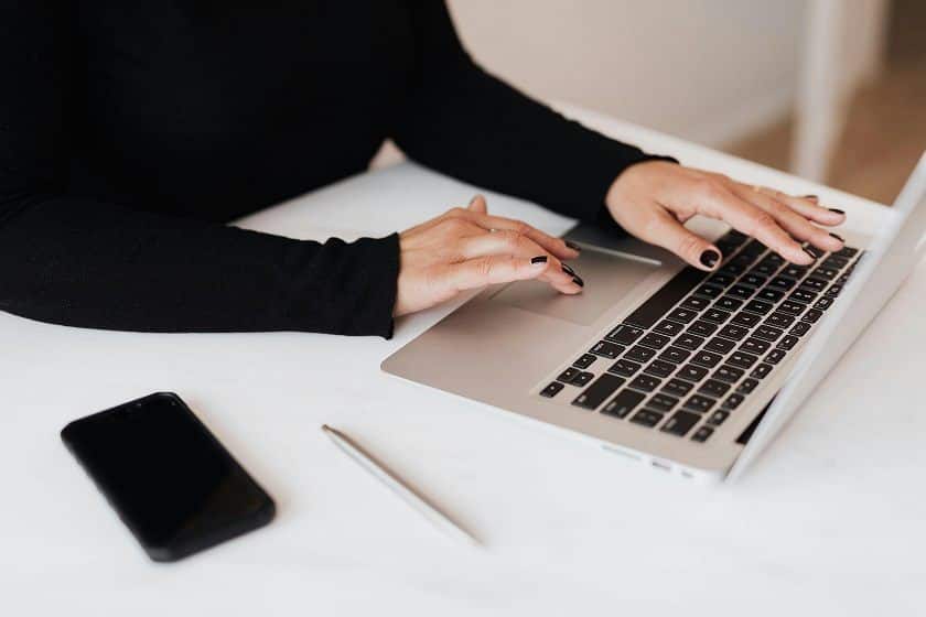 A woman's hands are seen using a computer keyboard. She's wearing a long-sleeved black shirt with black nail polish.