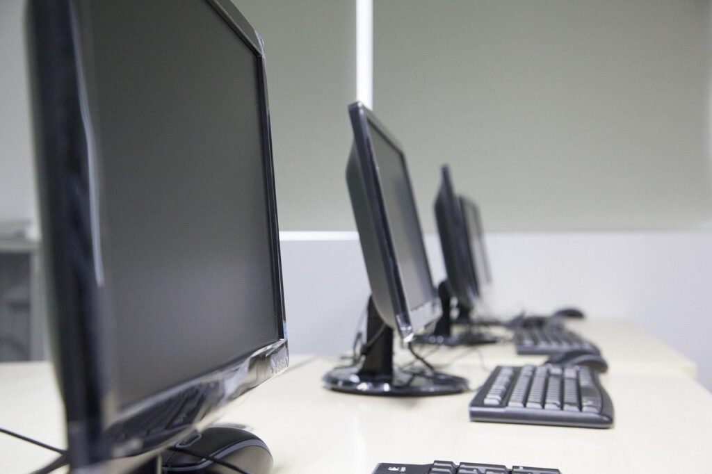 Three computer screens and keyboards sit in a row across a white desk.