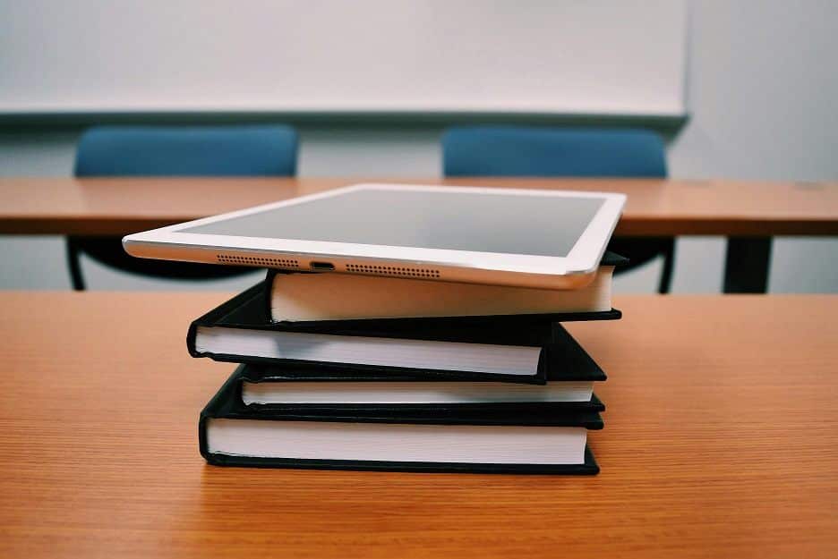 A computer tablet sits atop a stack of books on a school desk.