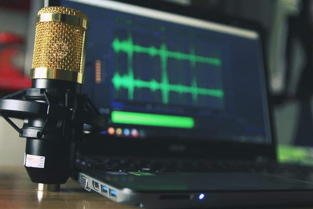 A closeup of an audio wave on a computer screen. A podcasting microphone is positioned in the foreground.