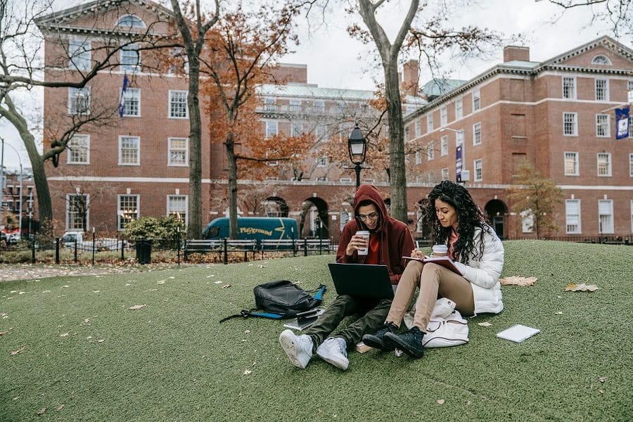 A man and a woman sit on the lawn in front of university building.