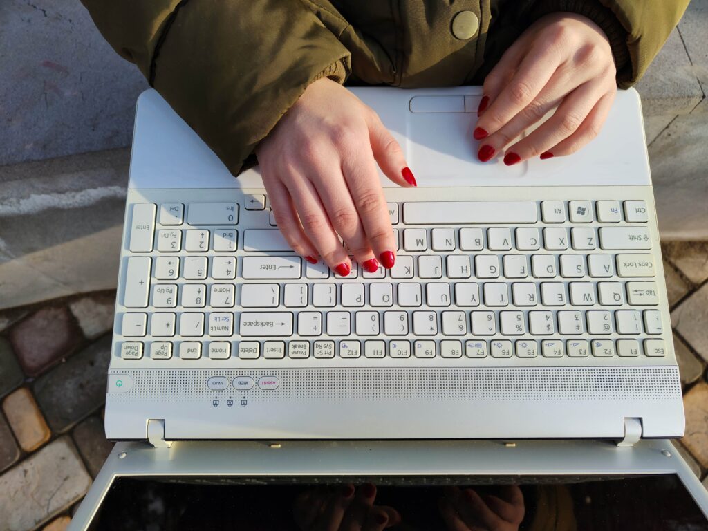 A white Mac laptop is shown open while a woman's hands with fingernails painted red are typing from it.