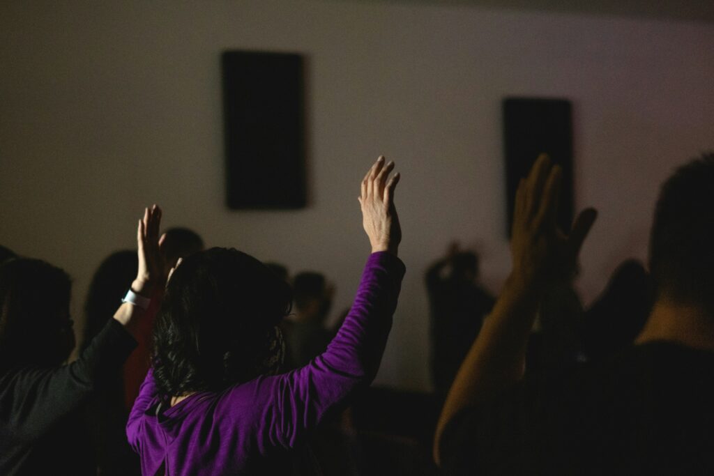 A religious setting shows a group of people with their hands raised in a prayer session