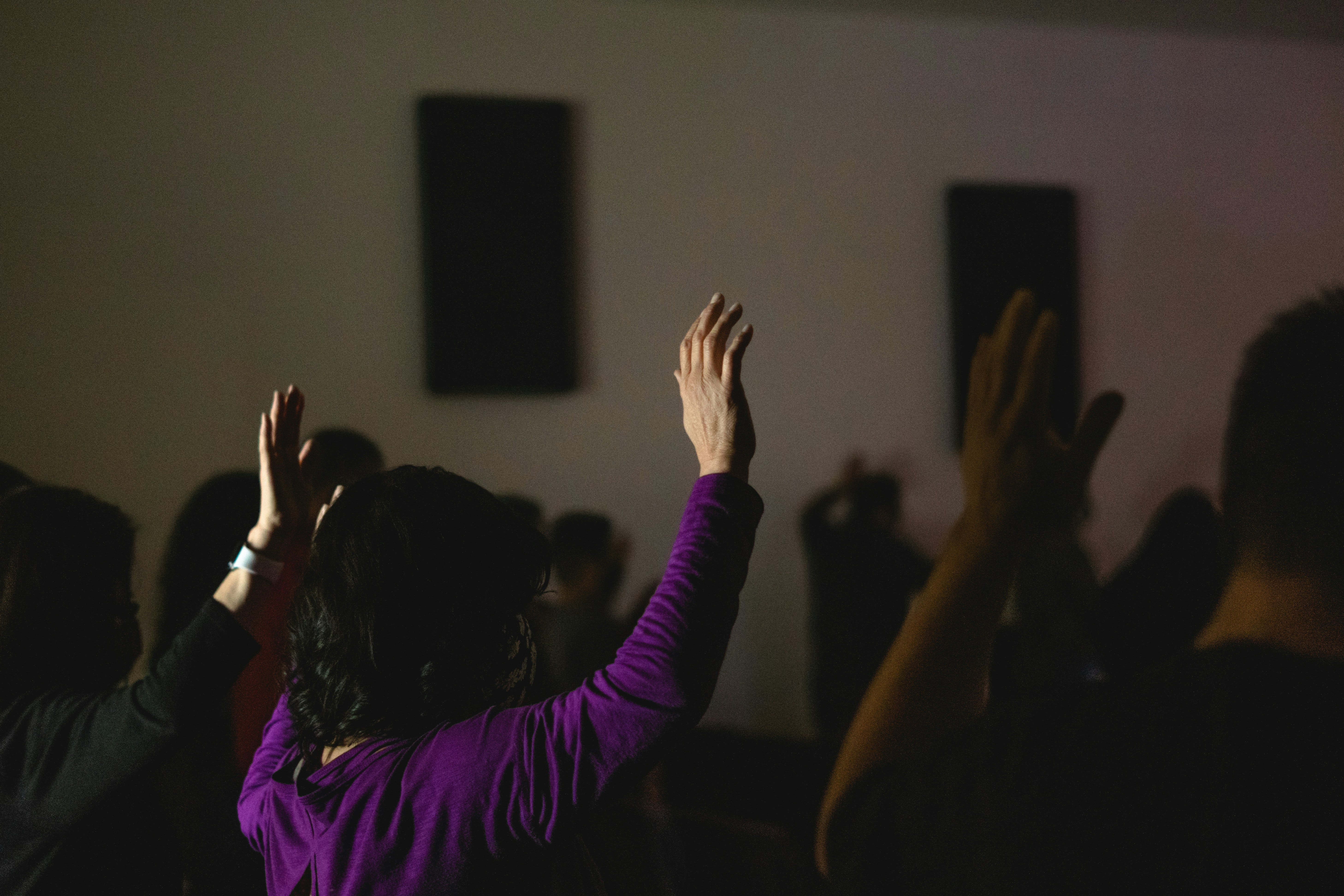 A religious setting shows a group of people with their hands raised in a prayer session