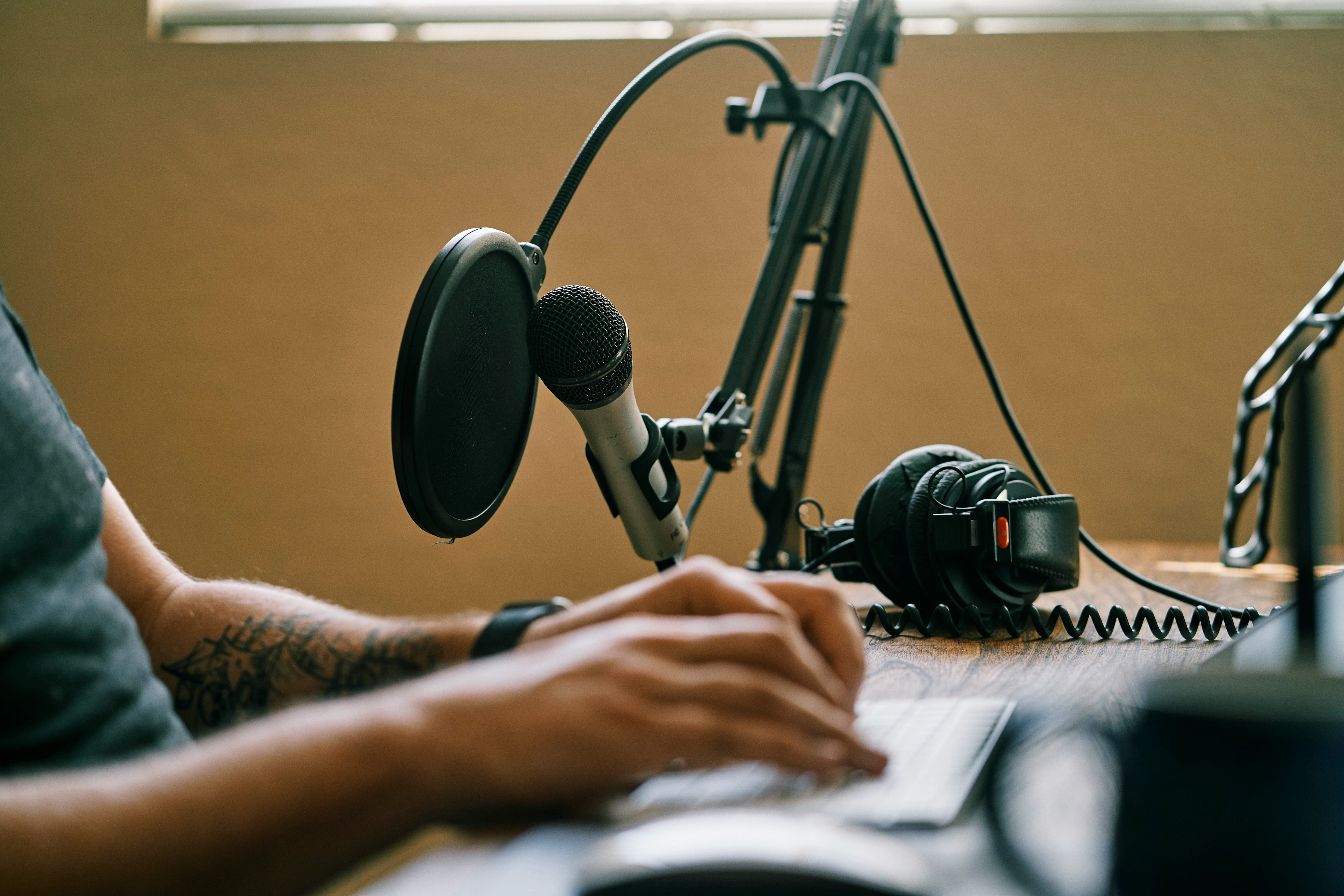 A man's hands are shown typing with a microphone and headset on the desk next to him