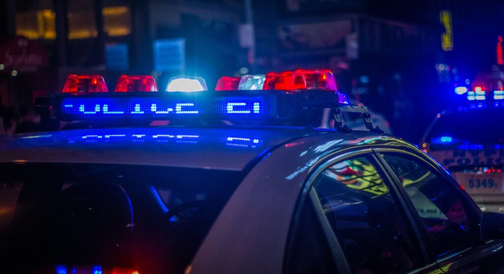 Blue and red headlights from the top of a police car are seen as it drives down a street