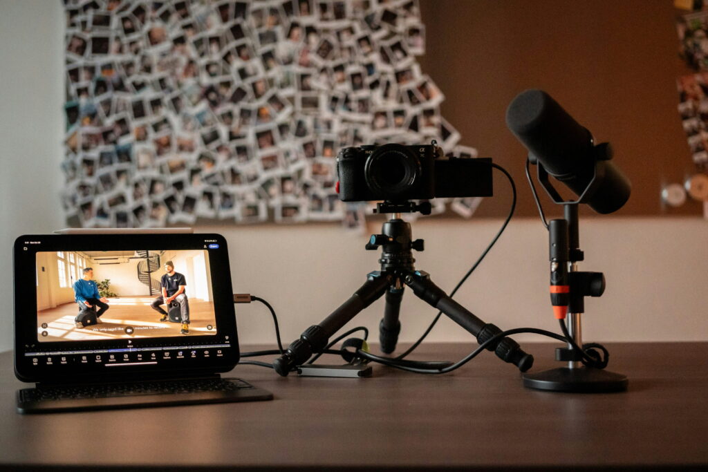 A video of two men sitting and engaging in conversation is shown on a device with a camera and microphone on stands on a desk to the right of it.