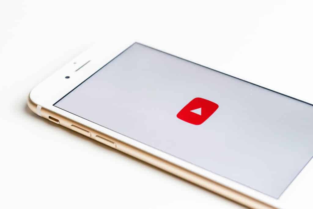 A white iPhone shows the YouTube red play button on-screen.