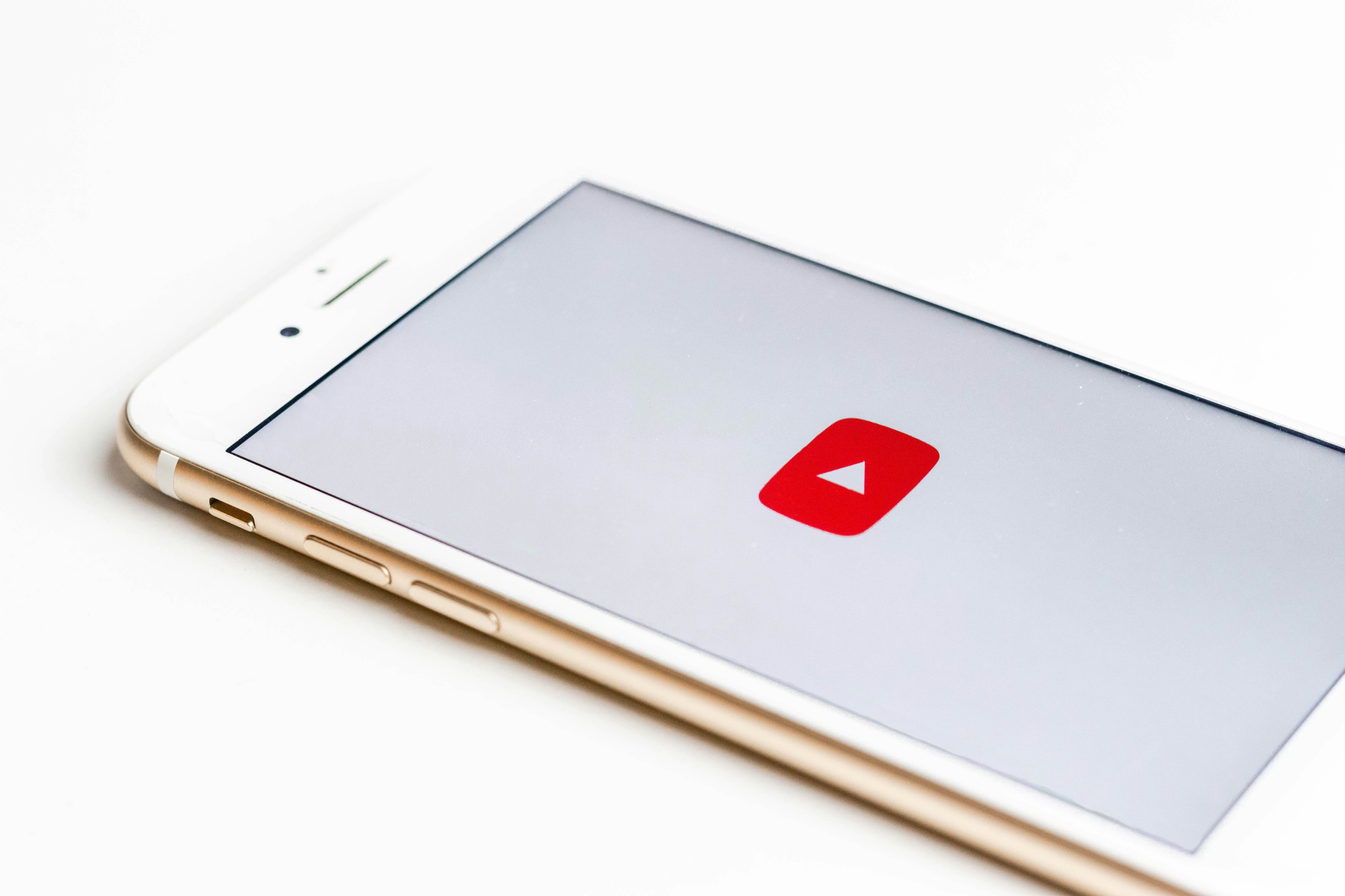 A white iPhone is shown on a flat surface with the red YouTube play button icon on its screen